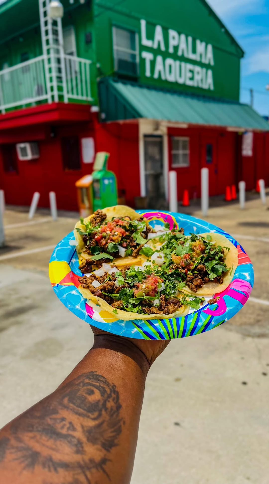 A plate of La Palma tacos held up in front of the taqueria